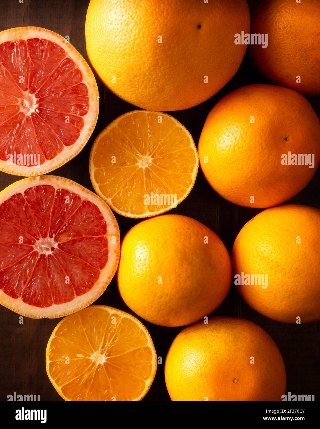 Draufsicht Bild von reifen Orange und Grapefruit Scheiben und Mehrere ganze Orangen auf braunem rustikalem Holztisch Stockfoto