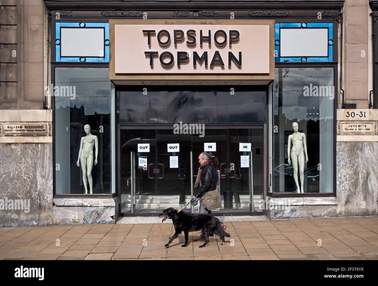 Mann, der mit seinem Hund am Eingang zum Topshop Topman Store in der Princes Street, Edinburgh, Schottland, Großbritannien, vorbeiläuft. Teil der gescheiterten Arcadia Group. Stockfoto