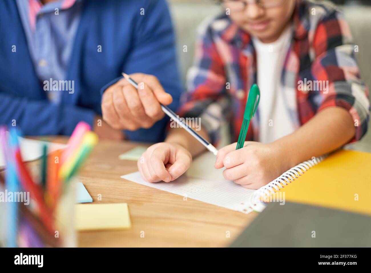 Nahaufnahme der Hände eines lateinischen Vaters mittleren Alters, der seinem Sohn, dem Schulkind bei den Hausaufgaben hilft, während er zu Hause am Schreibtisch sitzt Stockfoto