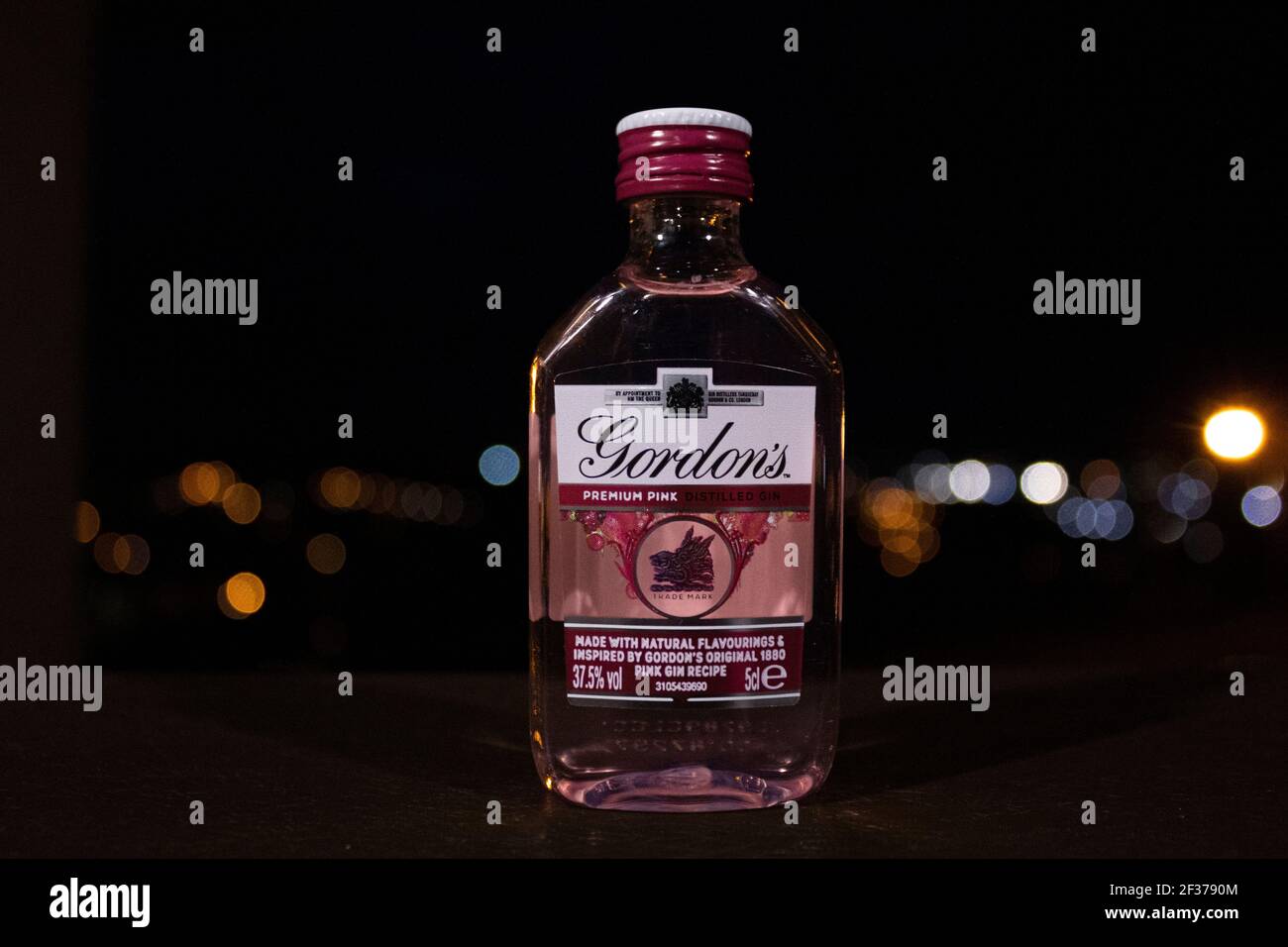 Kleine pinke Gin-Flasche mit Straßenlaternen dahinter, die verschwommen sind. Stockfoto