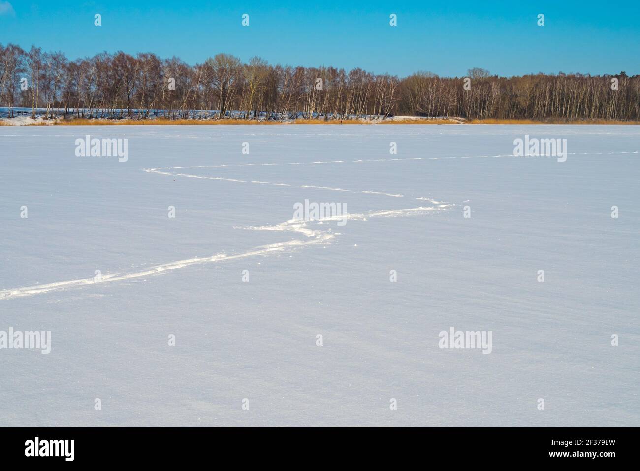 Fußspuren im Schnee, ein gefrorener schneebedeckter See und ein blauer Himmel Stockfoto