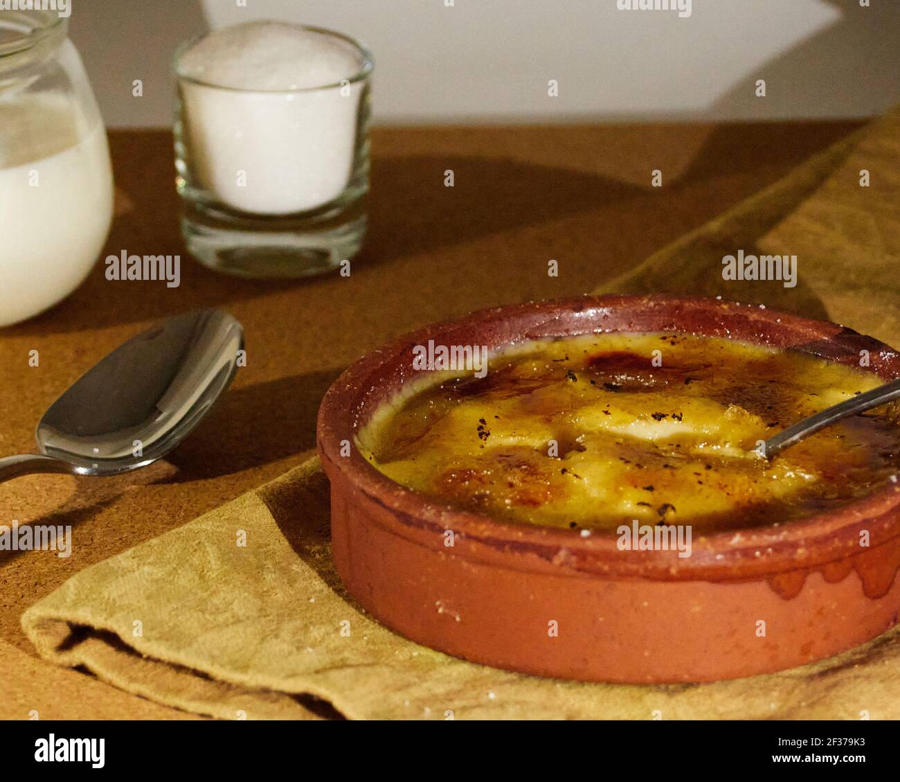 Löffel in katalanische Sahne getaucht auf einer Serviette mit einer Tasse Zucker und einer Tasse Milch dekoriert. Auf dem Holztisch Stockfoto