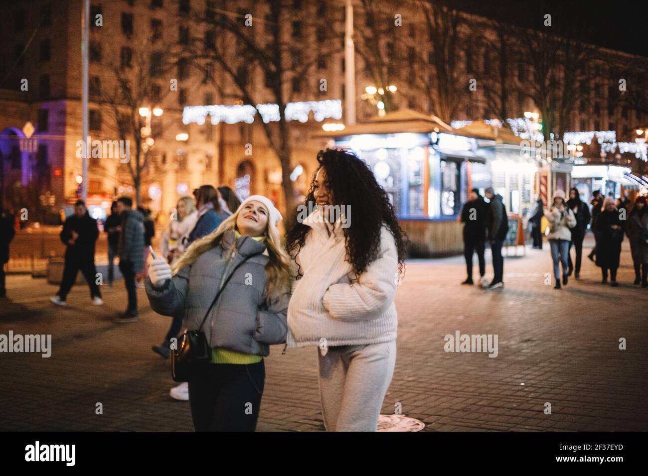 Glückliche Freundinnen, die nachts auf der Straße in der Stadt spazieren Im Winter Stockfoto