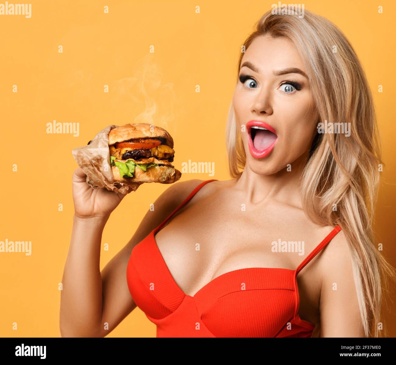 Frau halten große Cheeseburger Burger Sandwich mit offenem hungrigen Mund Überrascht glücklich schreiend lachend auf gelbem Hintergrund Stockfoto