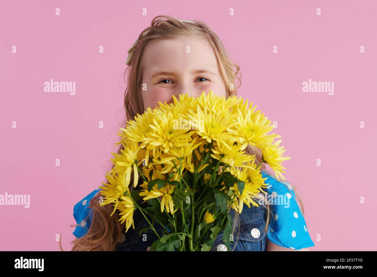 Happy stylish Mädchen in gepunkteten blau insgesamt mit gelben Chrysanthemen Blumen isoliert auf rosa Hintergrund. Stockfoto