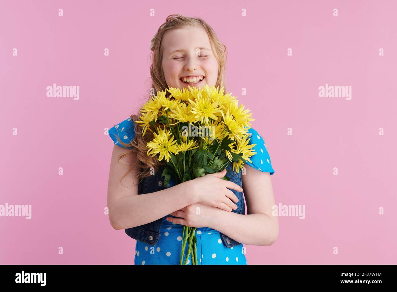Happy modernes Kind in gepunkteten blauen Overall mit gelben Chrysanthemen Blumen vor rosa Hintergrund. Stockfoto
