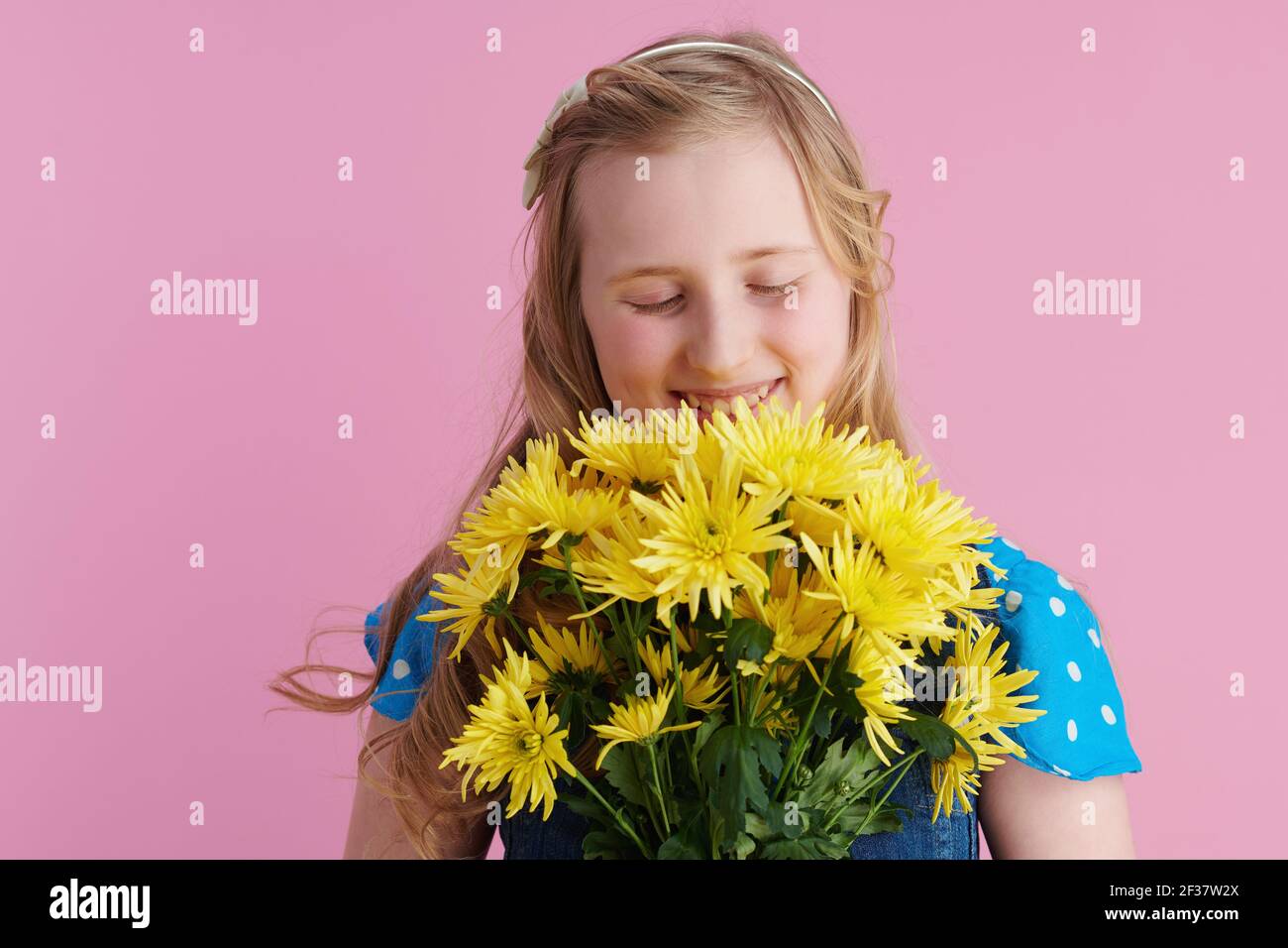 Entspannte stilvolle Mädchen mit langen welligen blonden Haaren mit gelben Chrysanthemen Blumen isoliert auf rosa Hintergrund. Stockfoto