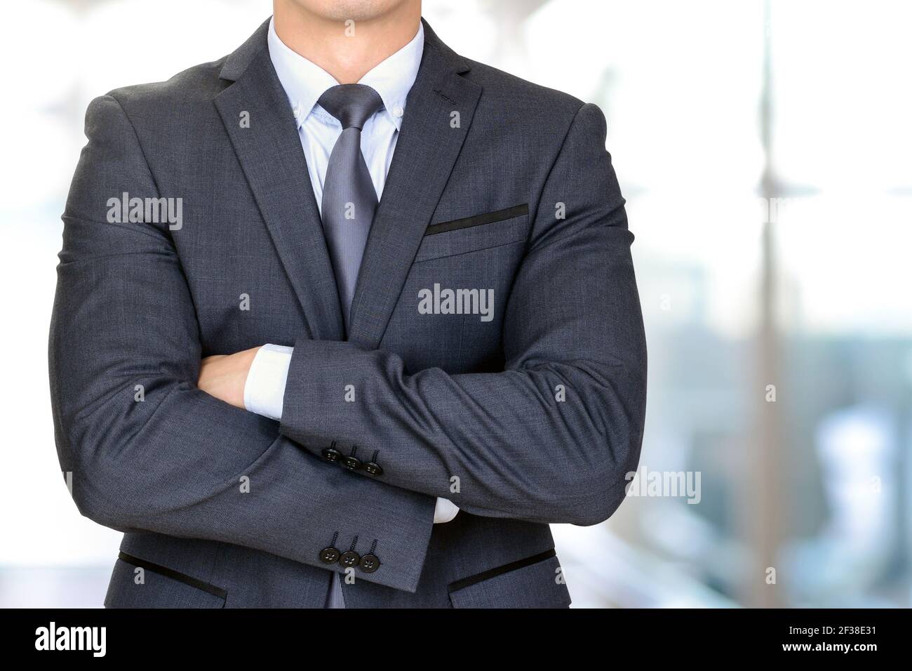Anonymer Geschäftsmann in dunkelgrauem Anzug, der seine Arme kreuzt Verwischen Sie den Hintergrund im Büroflur Stockfoto