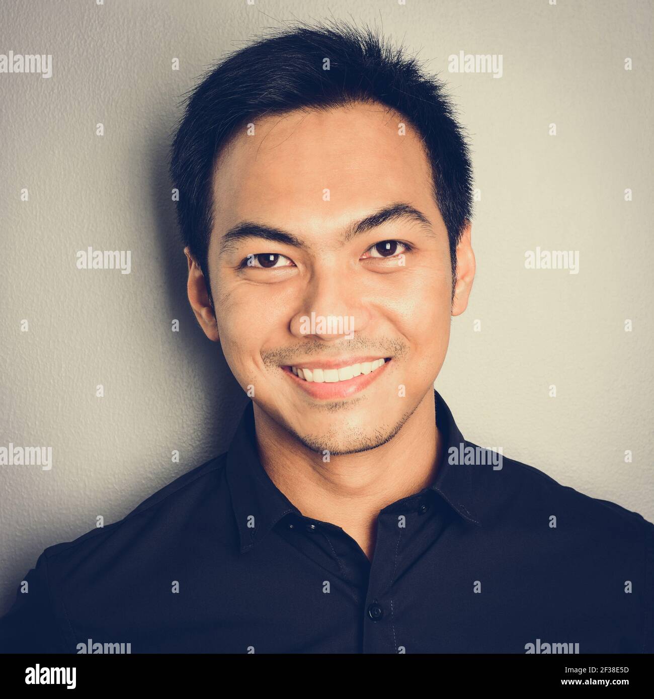 Attraktiver lächelnder asiatischer Mann auf hellgrauem Hintergrund - vintage Tone-Effekt Stockfoto