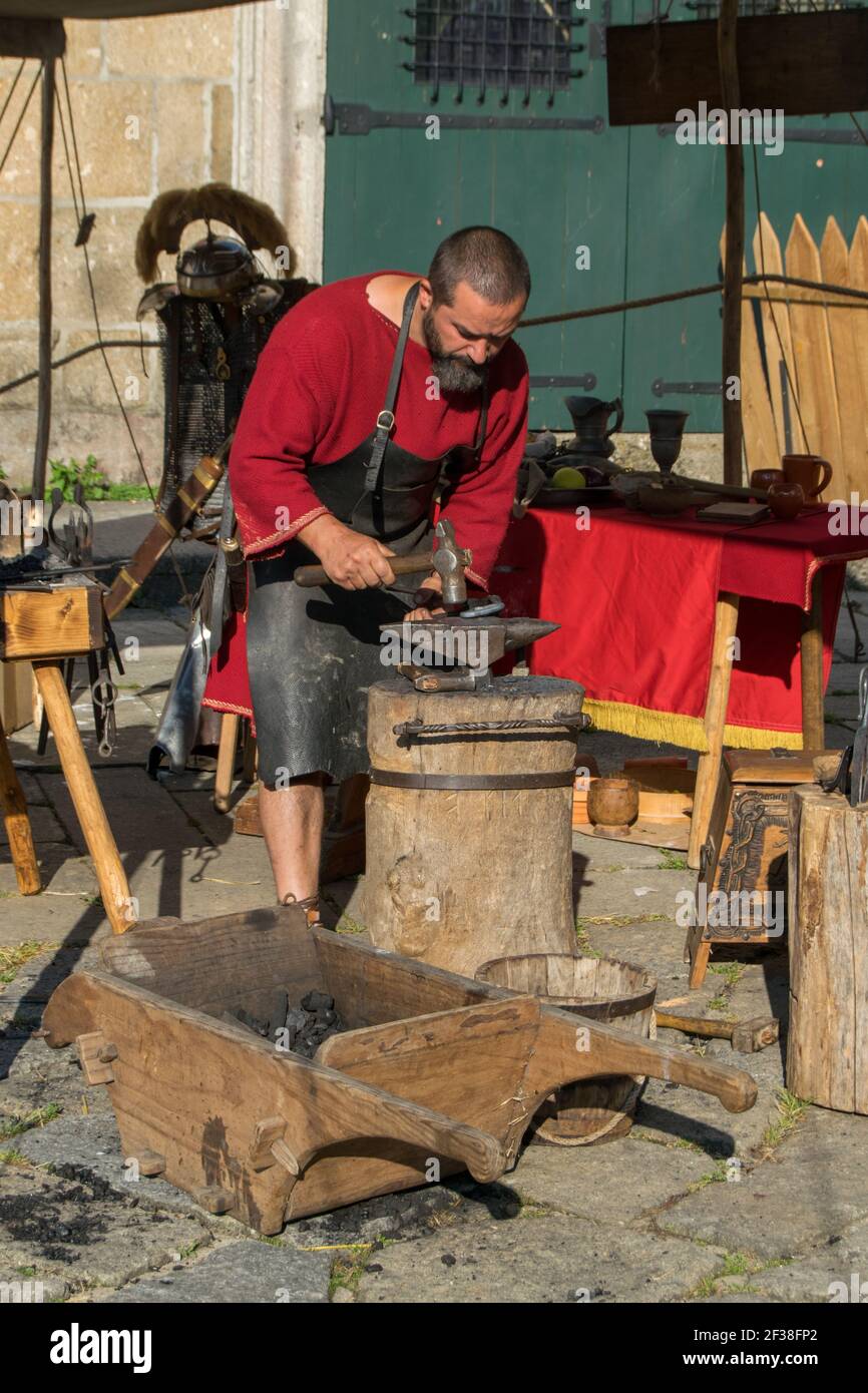 Schmied arbeitet mit angestammten Werkzeugen, römischen Lebensstil. Erholung. Mittelalterlicher Handwerker mit einem Hammer, der für kulturelle Vorführungen arbeitet Stockfoto