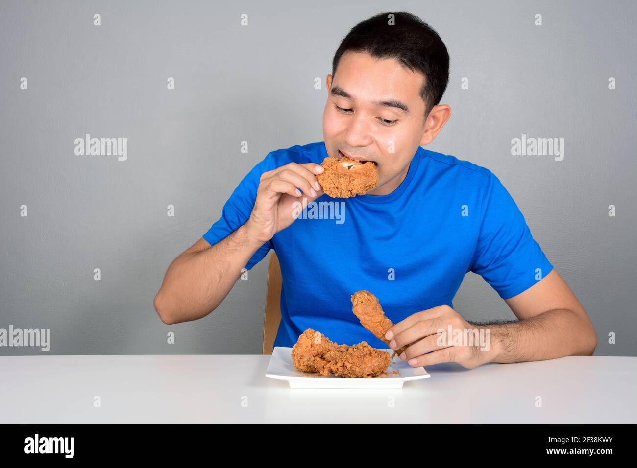 Junger Mann essen gebratenes Huhn auf dem Tisch Stockfoto