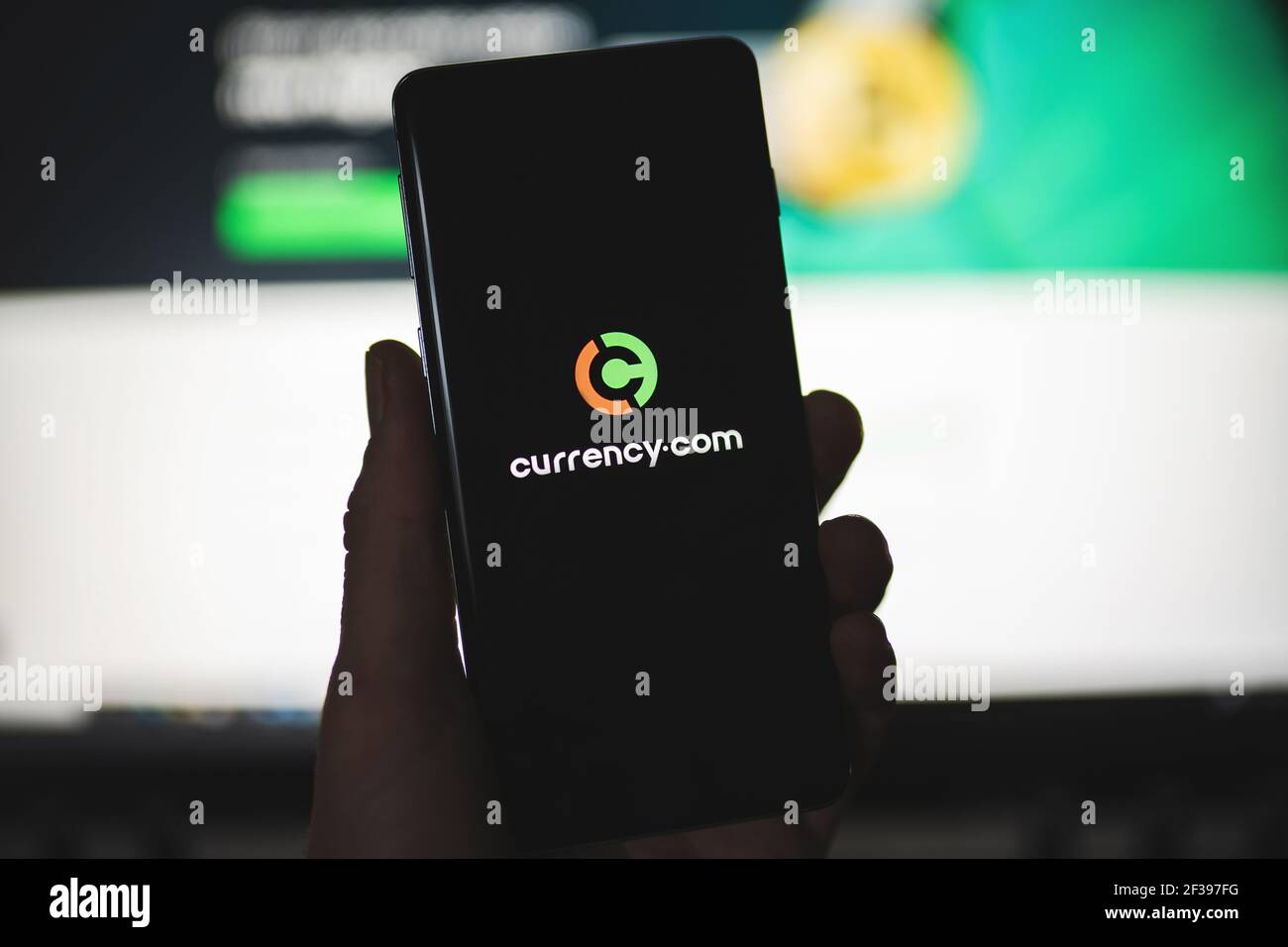 Smartphone mit Currency.com Logo mit verschwommener Website als Hintergrund. Handelsplattform, Aktien und Kryptowährungen Stockfoto