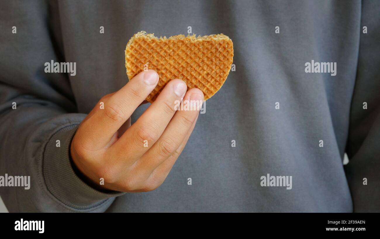 Junger Mann hält holländische Karamell Waffel traditionelle handgemachte Dessert grau sweatshirt im Hintergrund Stockfoto