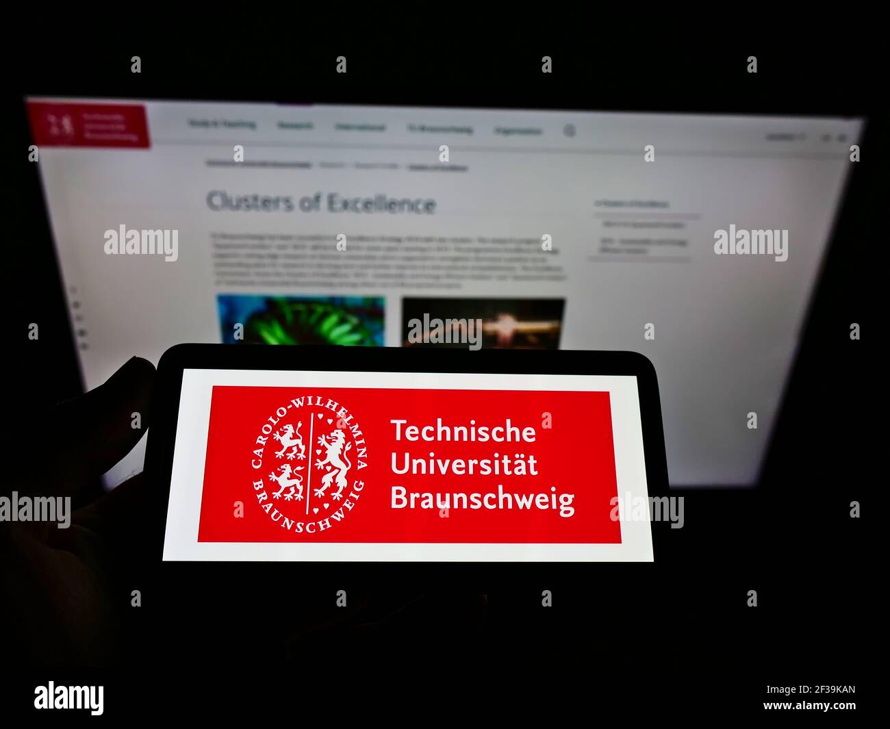Person, die Mobiltelefon mit Logo der TU Braunschweig auf dem Bildschirm vor der Webseite hält. Konzentrieren Sie sich auf die Telefonanzeige. Stockfoto