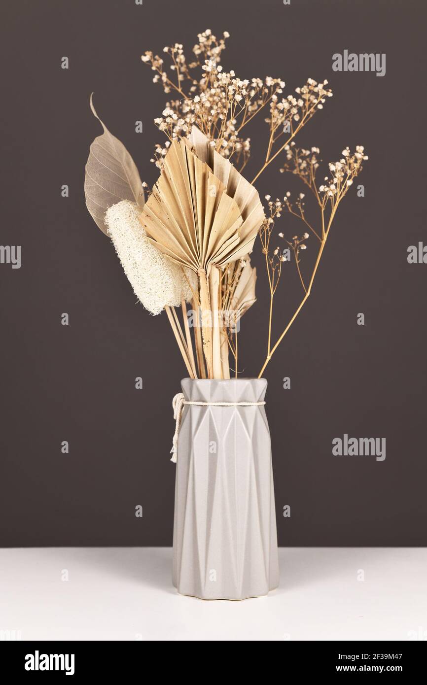 Natürliches Bouquet mit grauer Vase mit getrockneten Blüten und Blättern wie Palmblatt, Skelettblatt, Luffa und Gypsophila-Blüten Stockfoto