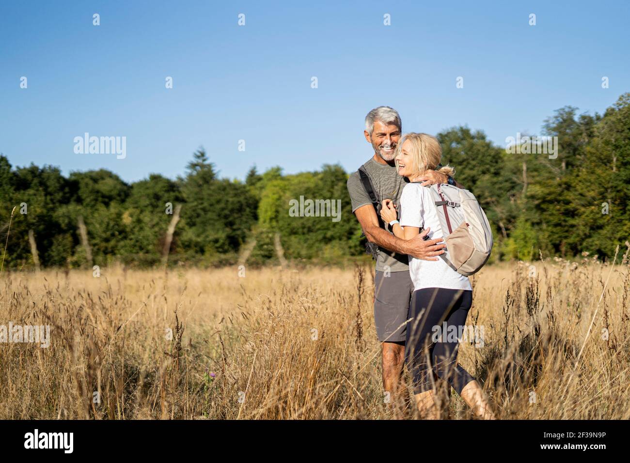 Lächelndes reifes Paar, das sich beim Wandern im Wald umarmt Stockfoto