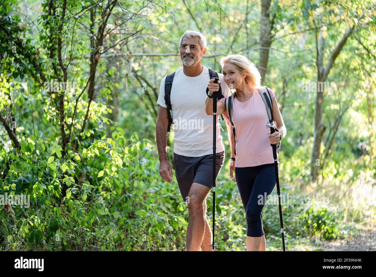 Lächelnde, reife Frau, die ihrem Mann beim Wandern im Wald die Richtung zeigt Stockfoto