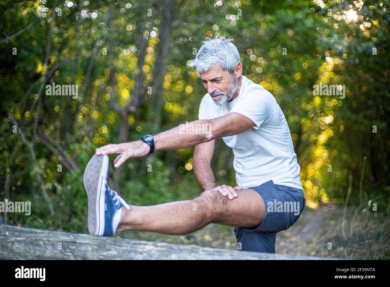 Reifer Mann, der sein Bein im Wald streckt Stockfoto
