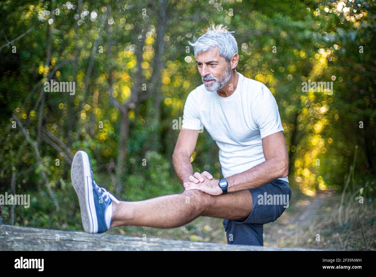 Reifer Mann, der sein Bein im Wald streckt Stockfoto