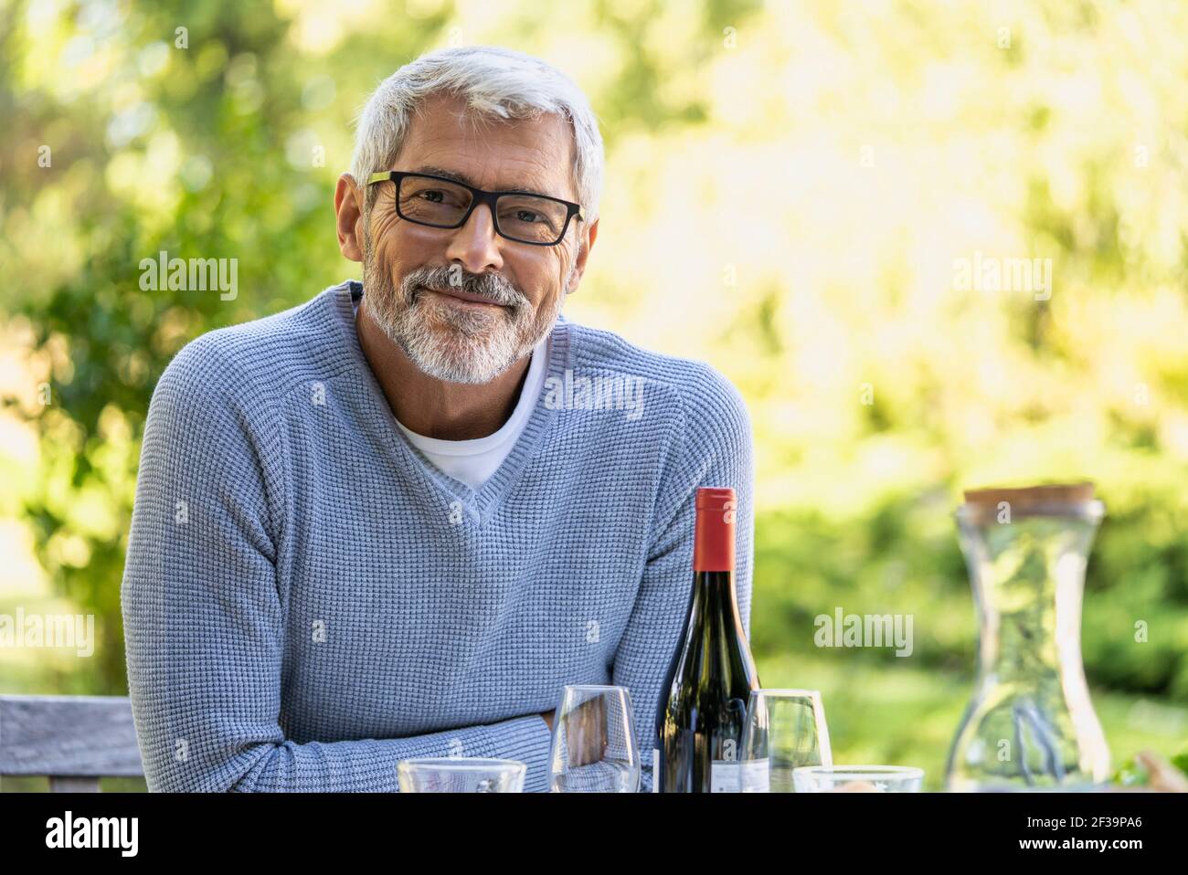 Porträt eines lächelnden, reifen Mannes, der sich im Hinterhof auf den Tisch lehnt Stockfoto