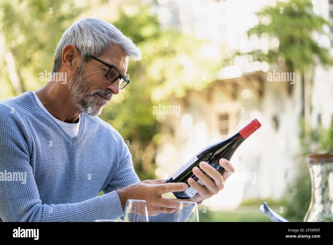 Reifer Mann, der Weinflasche ansieht, während er auf einem Stuhl sitzt Stockfoto