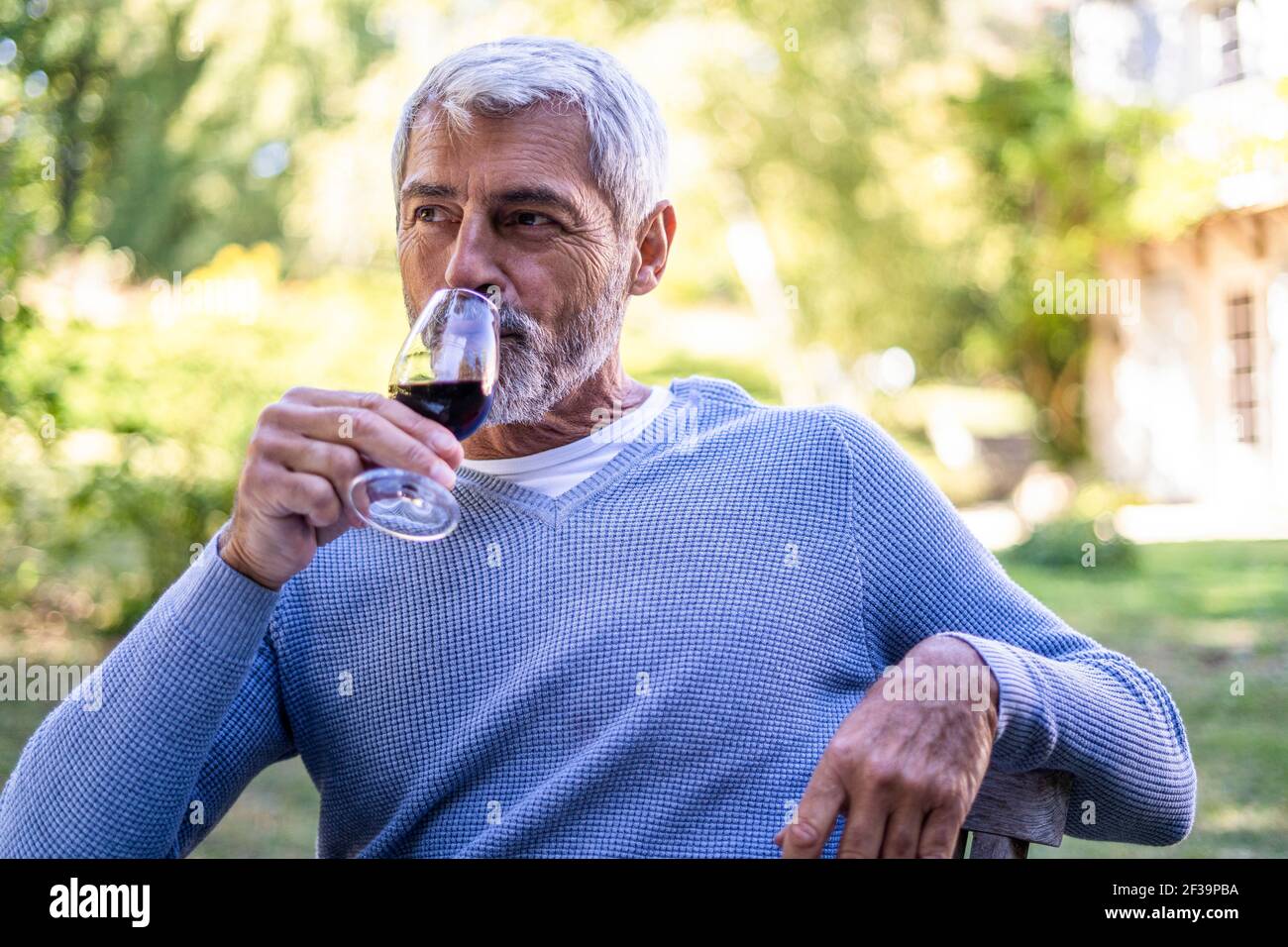 Reifer Mann trinkt Rotwein, während er auf einem Stuhl sitzt Stockfoto