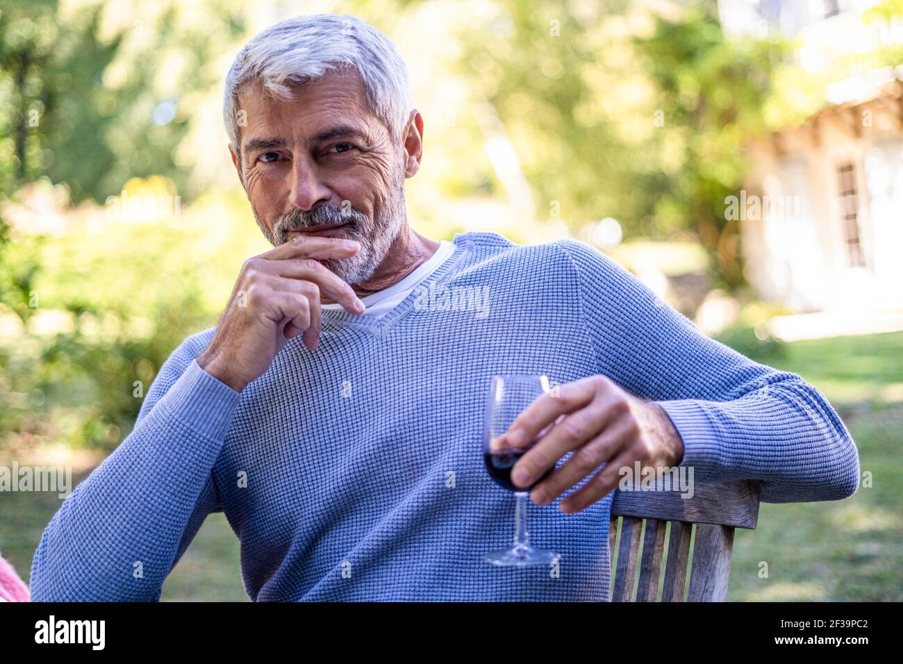Porträt eines reifen Mannes, der Weinglas hält, während er auf einem Stuhl sitzt Stockfoto