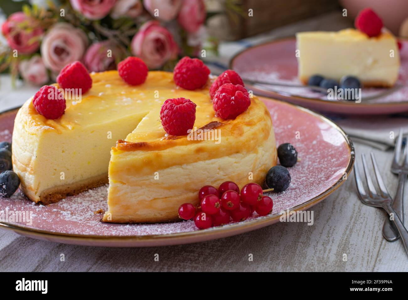 Tisch in blassrosa Farbe mit Käsekuchen, Blumen und Gabeln Stockfoto