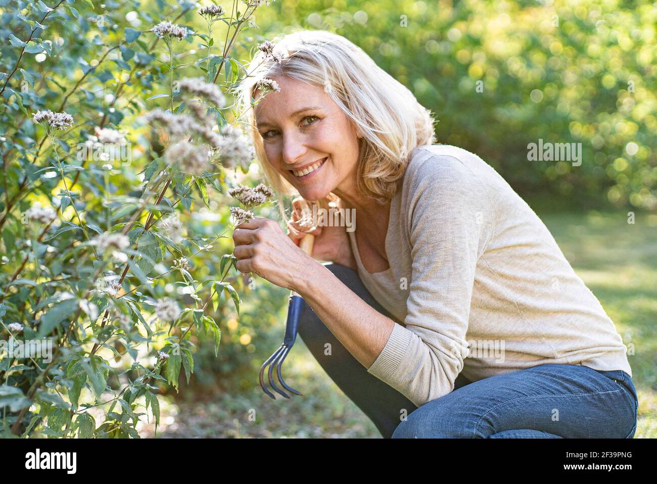 Porträt einer lächelnden reifen Frau, die Blumen im Hinterhof riecht Stockfoto