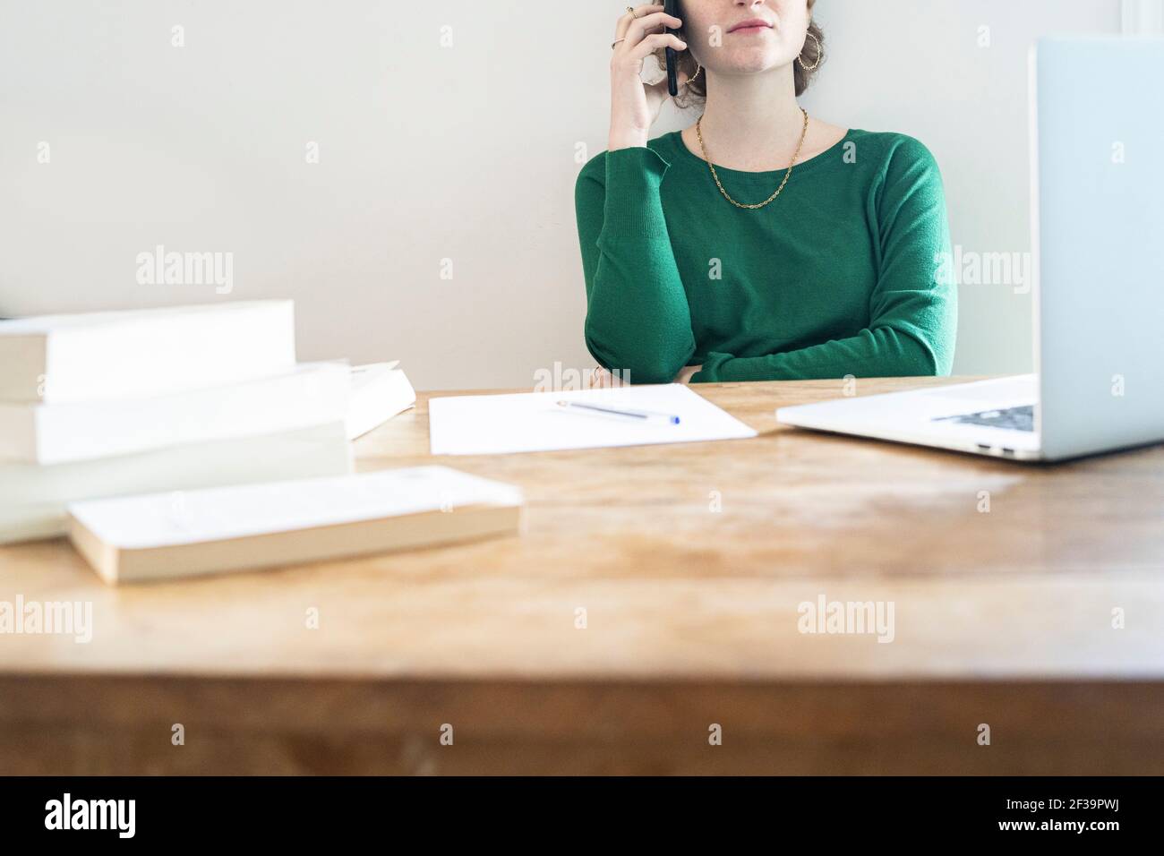 Mittlerer Abschnitt einer Frau, die auf dem Smartphone spricht, während sie zu Hause vor dem Laptop sitzt Stockfoto