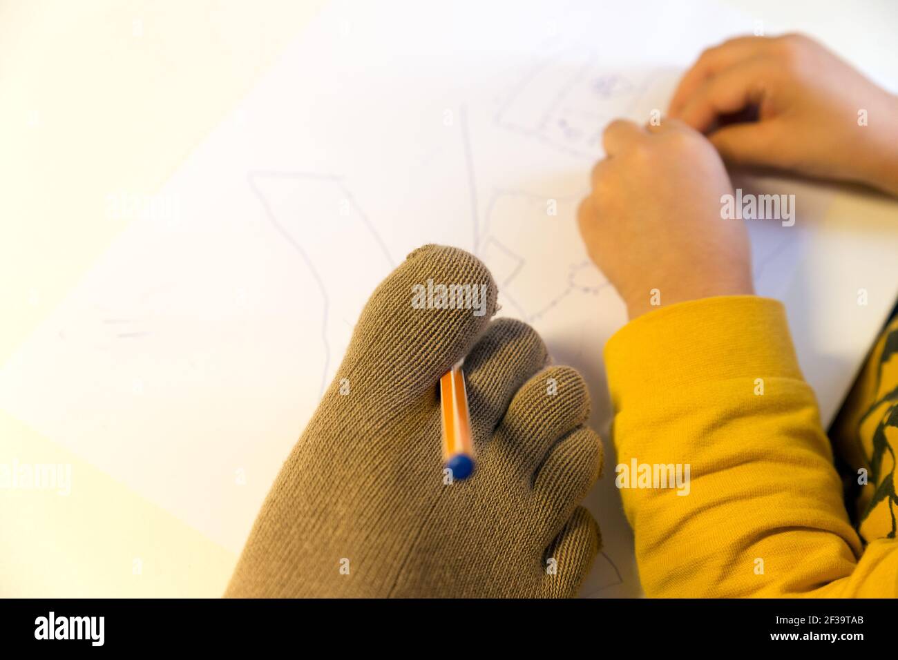 Ein Erwachsenenfuß mit Zehensocken hält einen Stift, begleitet von den Händen eines Kleinkindes, und zeichnet etwas. Behinderte Eltern, Körperpositivität, kreative Kinderbetreuung Stockfoto