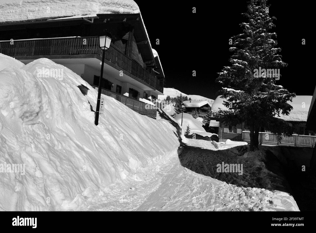 Monochrom von Chalets unter tiefem Schnee auf einem Schnee bedeckt Lane mit blauem Himmel in einem Skigebiet Stockfoto