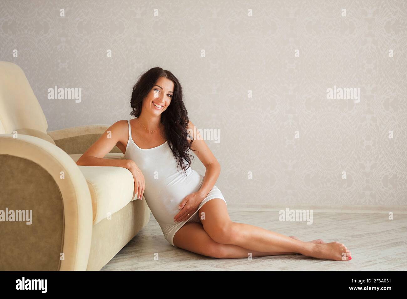 Schöne schwangere Frau zu Hause. Junge schwangere Frau sitzt auf dem Bett und berührt ihren Bauch. Schwangerschaftskonzept. Stockfoto