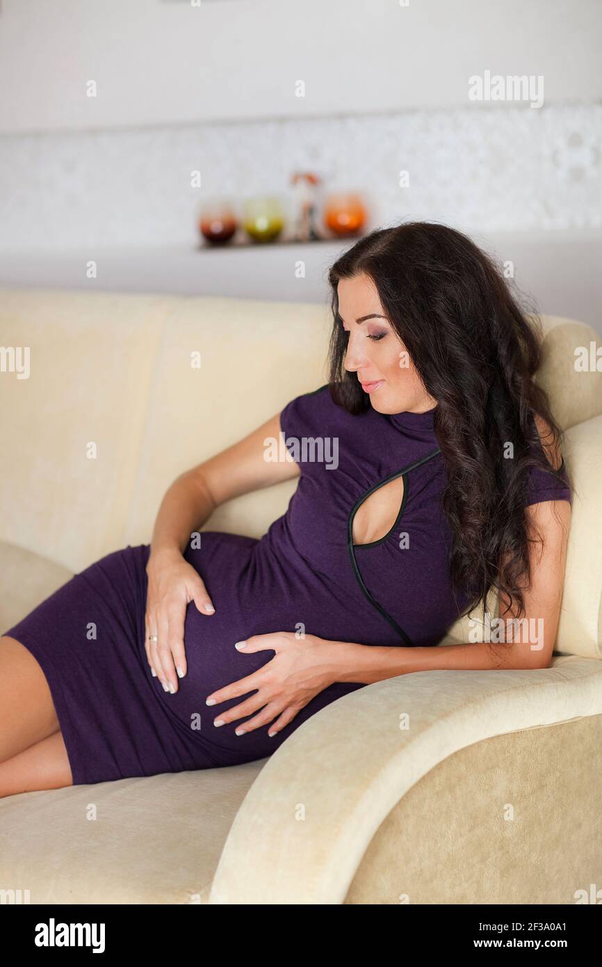 Schöne schwangere Frau zu Hause. Junge schwangere Frau sitzt auf dem Bett und berührt ihren Bauch. Schwangerschaftskonzept. Stockfoto