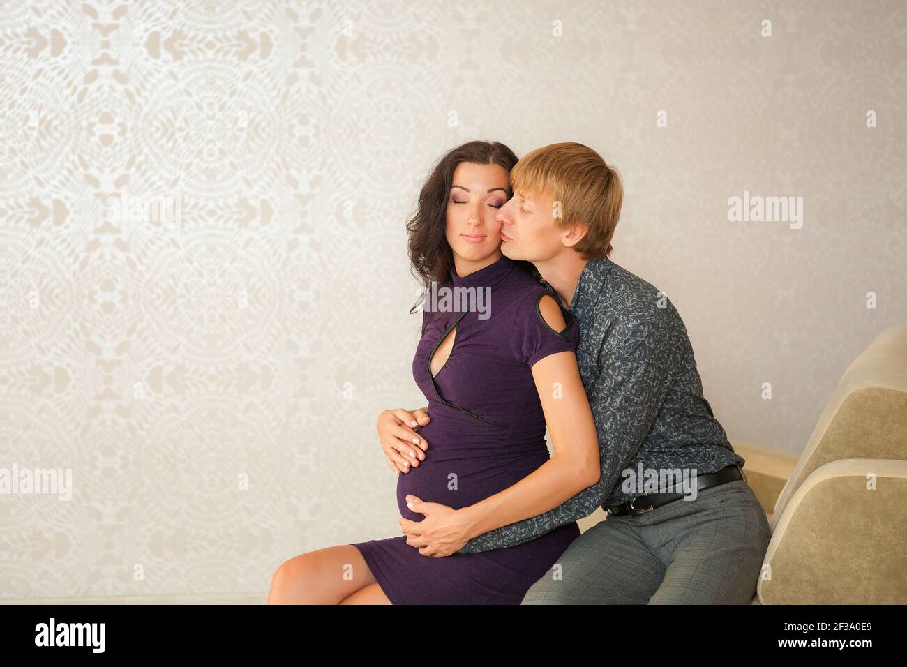 Junges Paar mit schwangeren Frau zu Hause entspannen. Glücklicher Mann umarmt seine schwangere Frau auf dem Sofa. Speicherplatz kopieren. Schwangerschaft und Menschen Konzept. Stockfoto