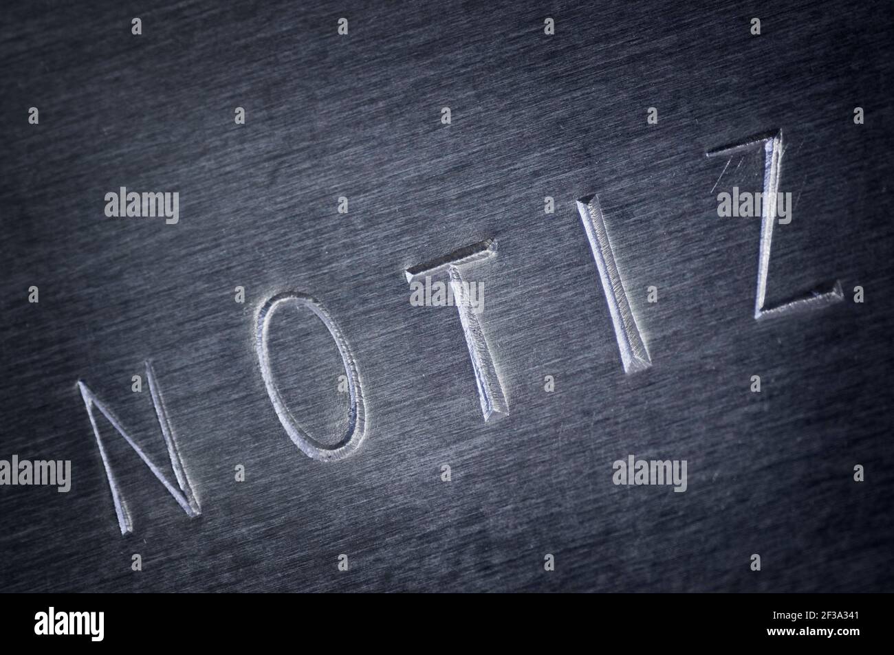 Nahaufnahme einer grauen abgeschrägten Metallplatte mit dem Wort NOTE diagonal eingestanzt. Stockfoto