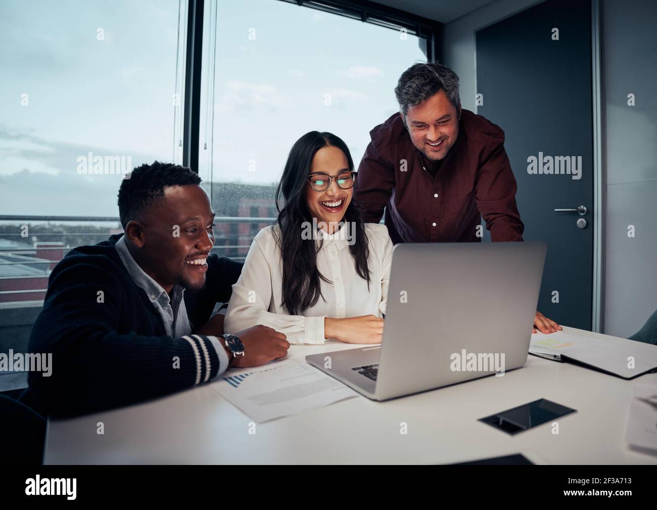 Glückliche, multiethnische Gruppe von Geschäftsleuten, die sich über Laptops unterhalten Neues Projekt im Büro Stockfoto