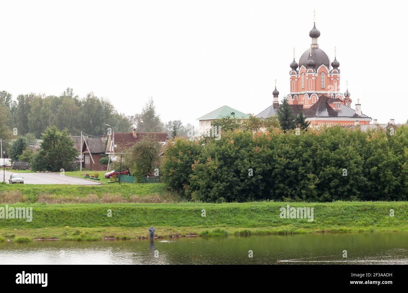Tichwin, Russland - 6. September 2020: Küstenlandschaft Tichwins, Russland mit einem Fischer. Kathedrale von Dormition unter bewölktem Himmel an einem Tag Stockfoto