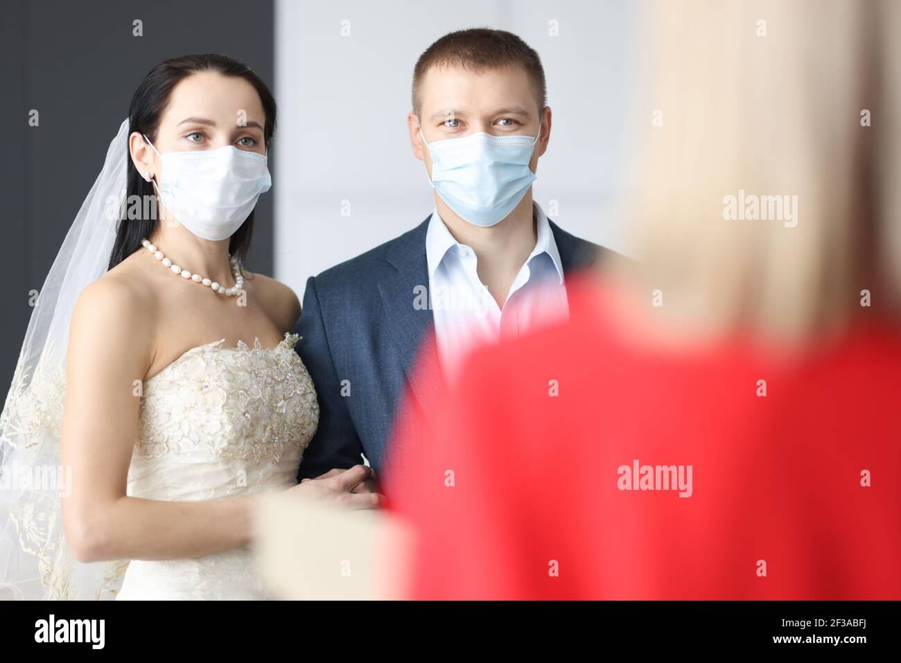 Braut und Bräutigam tragen medizinische Schutzmasken stehen vor Der Empfangsdame Stockfoto
