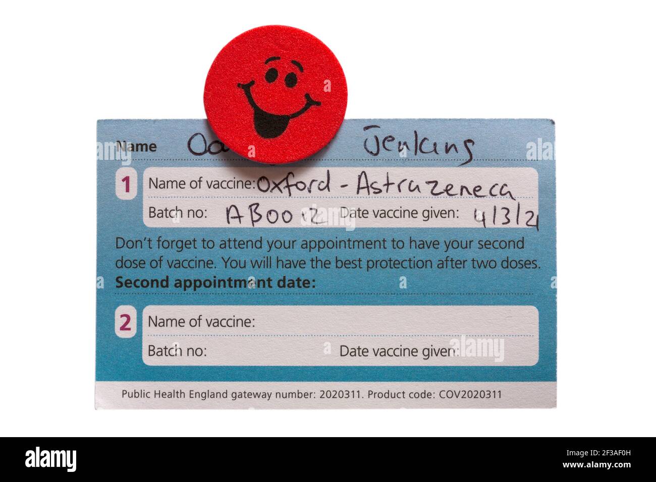 COVID-19-Impfkarte, ausgestellt vom NHS für Oxford AstraZeneca-Impfstoff, Oxford Astra Zeneca-Impfstoff mit Smiley-Face-Emoji-Aufkleber Stockfoto