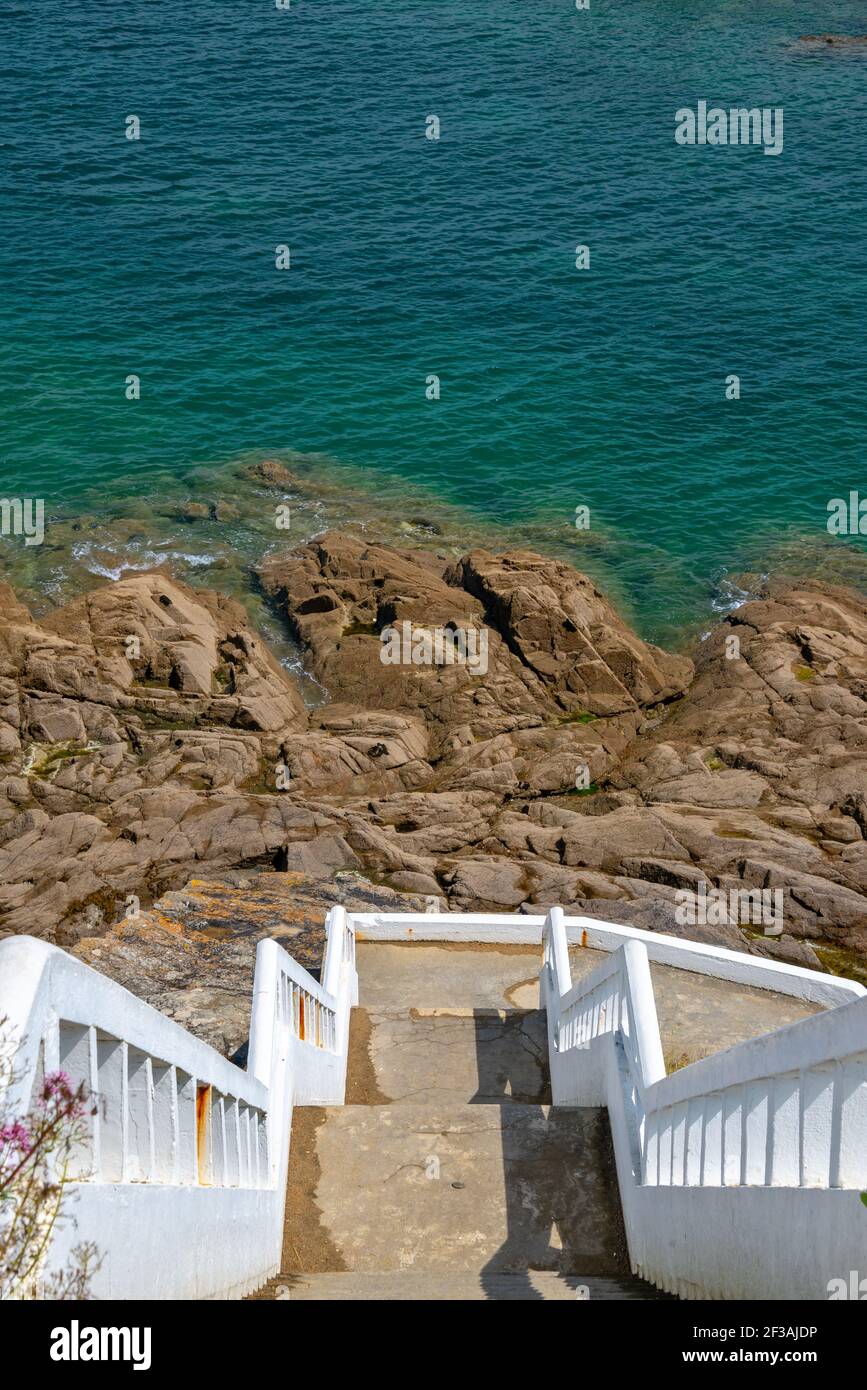 Weiße Treppen hinunter zu Felsen und blauem Meer. Vertikaler Meereshintergrund Stockfoto