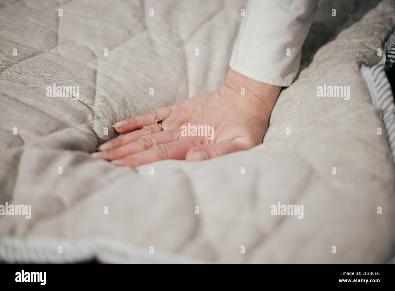 Frauenhand drückt auf weiße Matratze. Härte und Weichheit prüfen. Leere Stelle für Text oder Logo. Draufsicht. Nahaufnahme. Stockfoto
