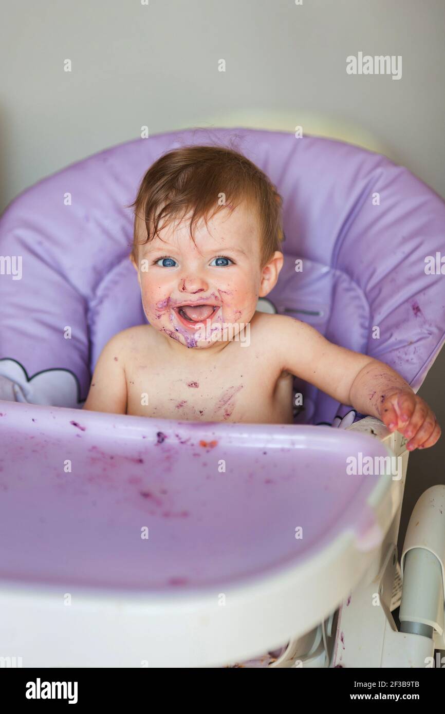 Adorable Baby essen auf Babystuhl und machen ein Durcheinander. Kleines Mädchen essen Essen in der Küche. Stockfoto