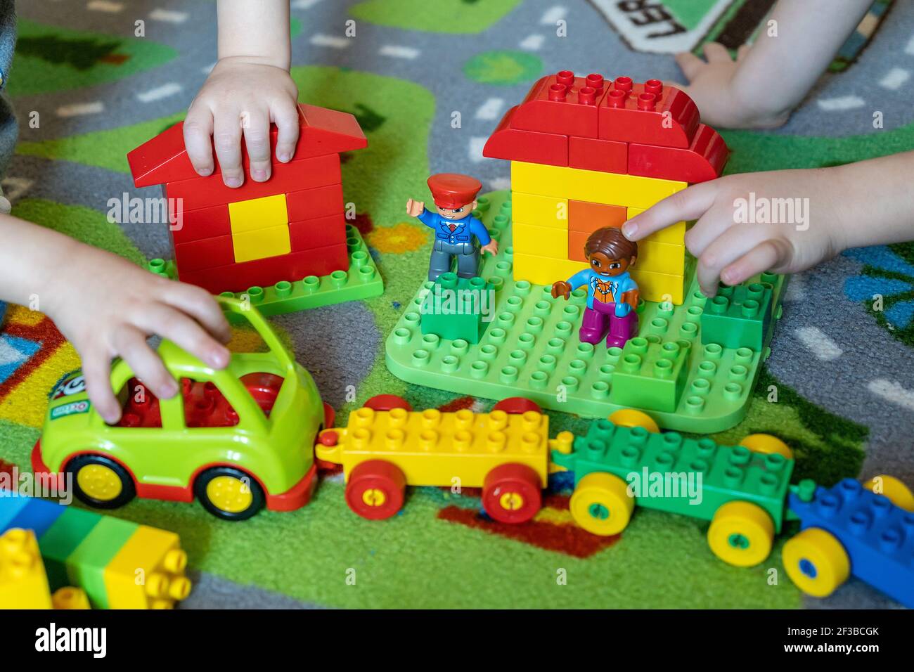 Nahaufnahme von Kinderhände, die mit bunten Plastikziegeln auf einem bunten Teppich spielen. Stockfoto