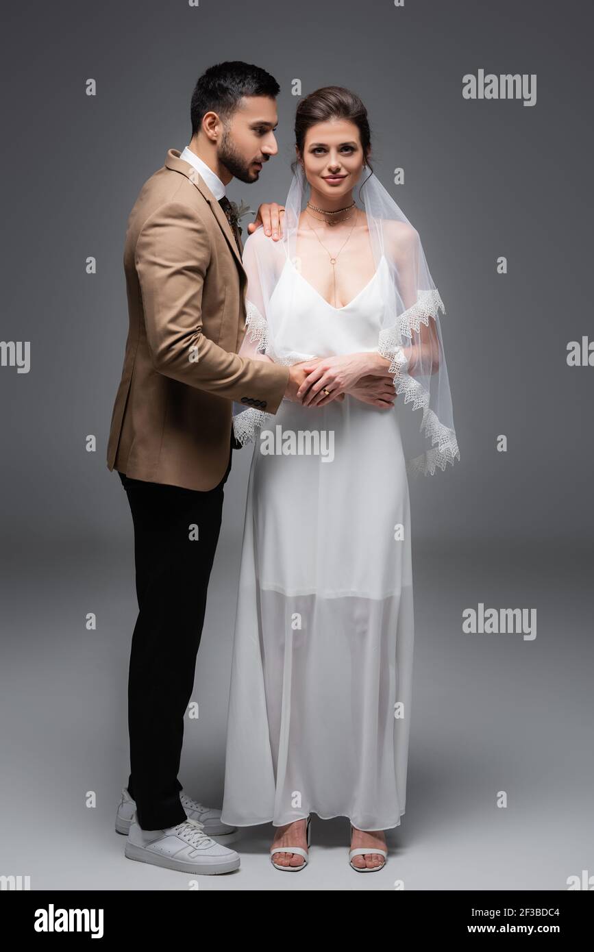 Gluckliche Braut Im Hochzeitskleid Blick Auf Kamera In Der Nahe Von Muslim Brautigam Auf Grau Stockfotografie Alamy