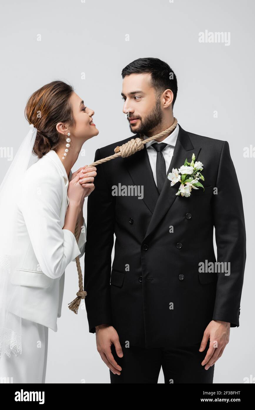 Lächelnde Braut zieht Slip Knoten am Hals des arabischen Bräutigam Isoliert auf Grau Stockfoto