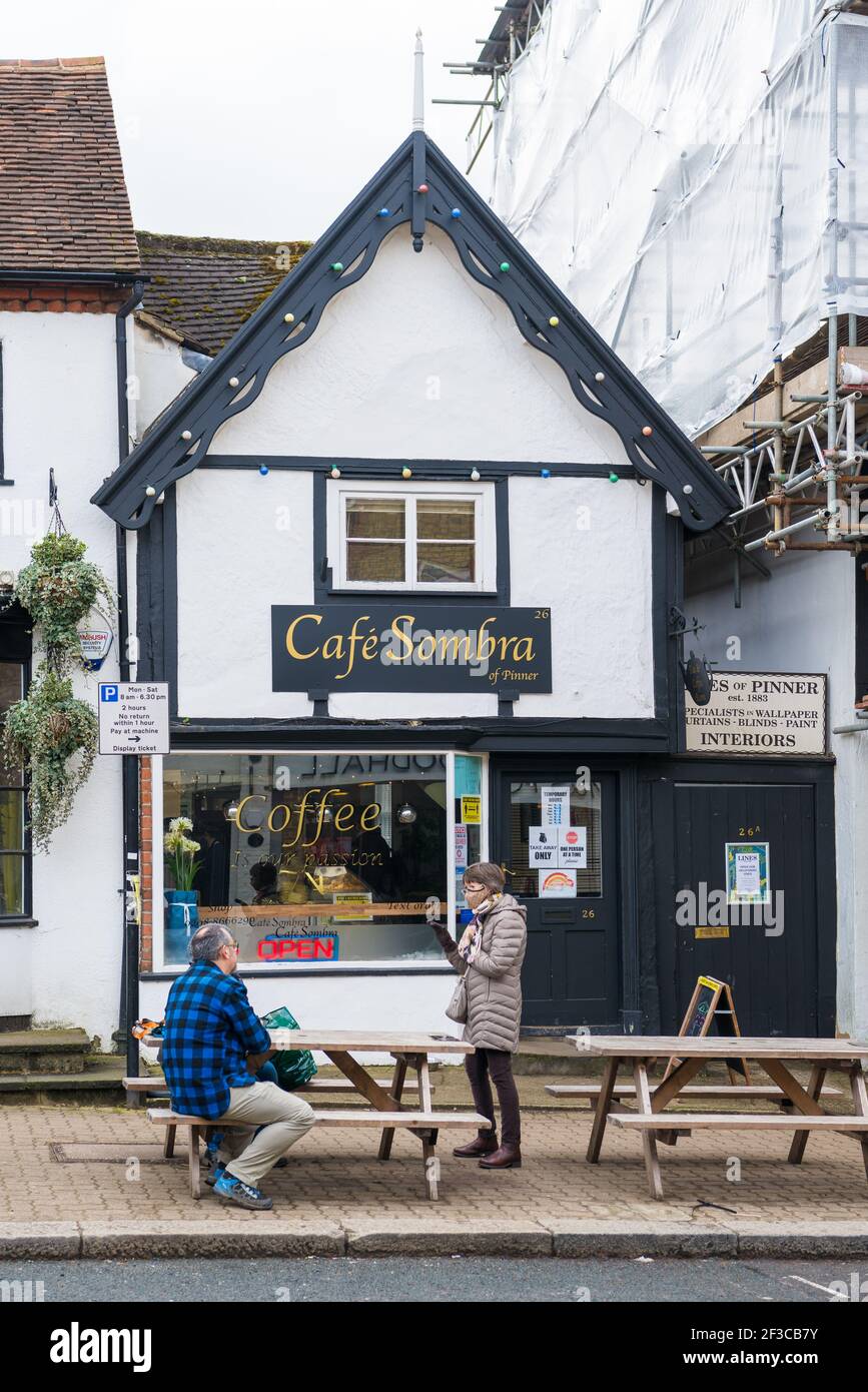Ein Paar saß an einem Gehsteig Tisch im Gespräch mit einer stehenden Frau trägt eine Gesichtsmaske vor dem Cafe Sombra Café, High Street, Pinner. Stockfoto
