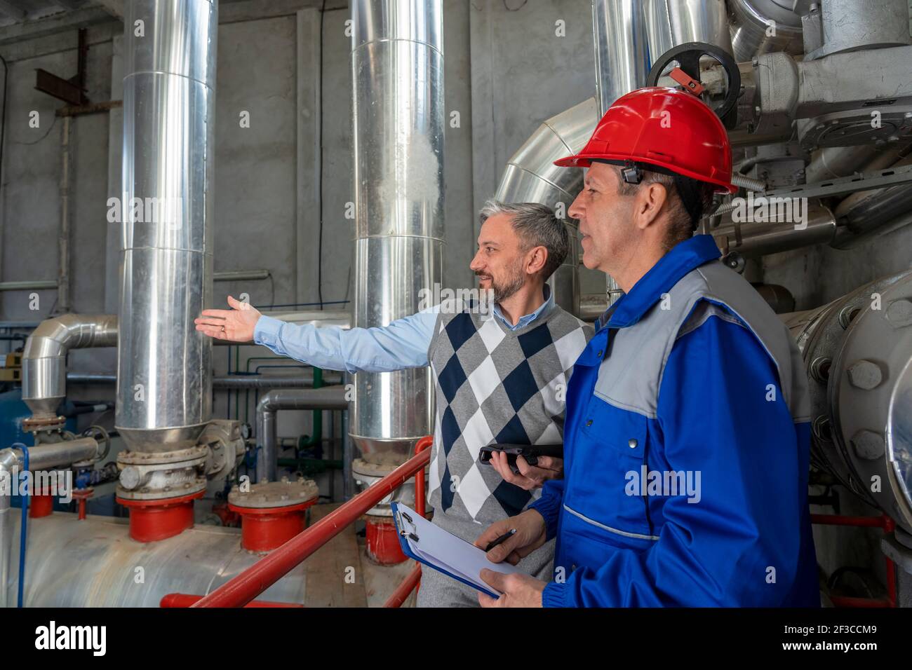 Wartungstechniker und Geschäftsleute im industriellen Innenraum mit großen Rohrleitungen. Industrie 4,0 Stockfoto