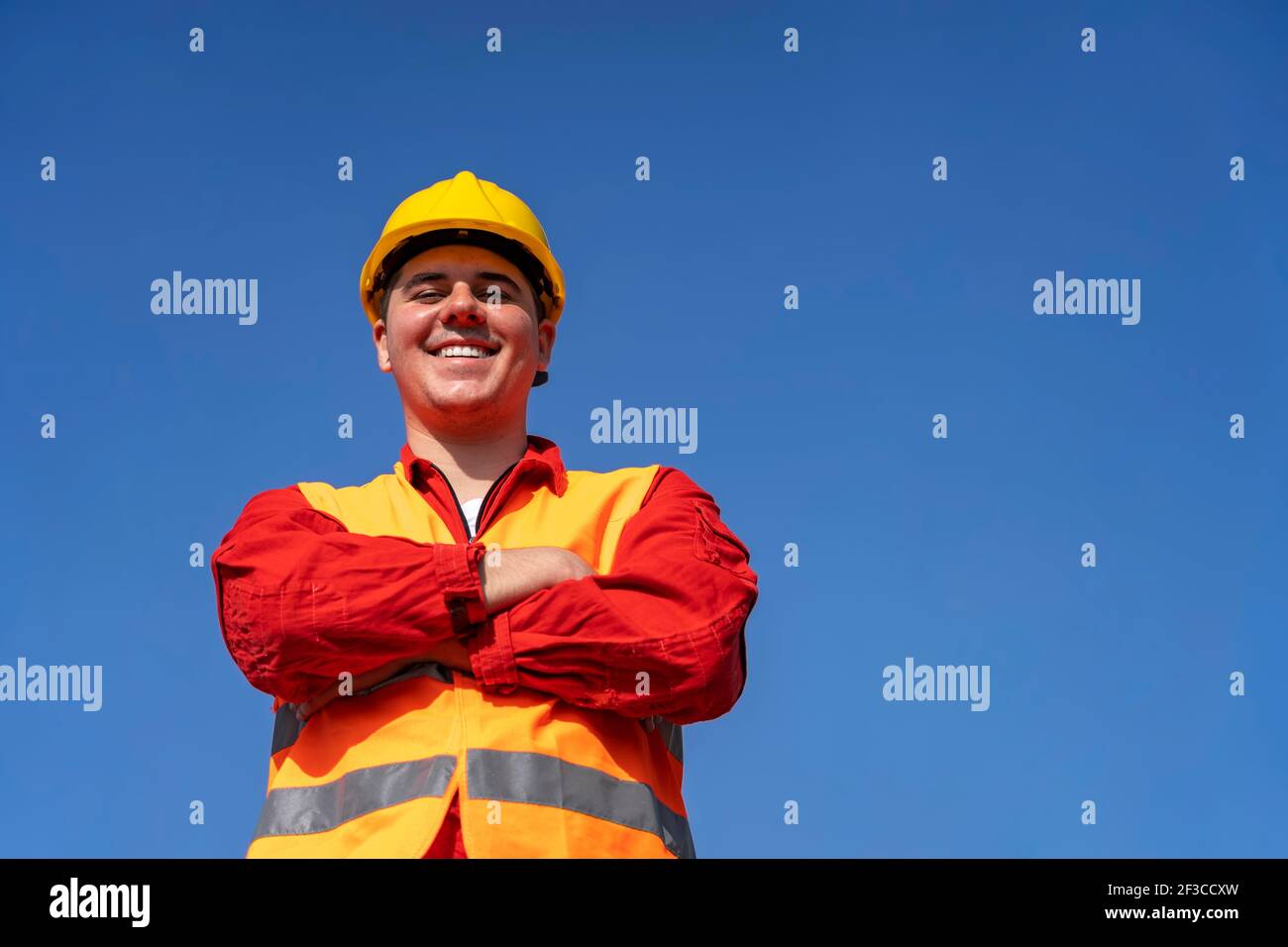 Selbstbewusster junger Arbeiter in reflektierender Kleidung und gelber Hardhat. Portrait eines lächelnden Bauarbeiters oder Ölarbeiters in persönlicher Schutzausrüstung. Stockfoto