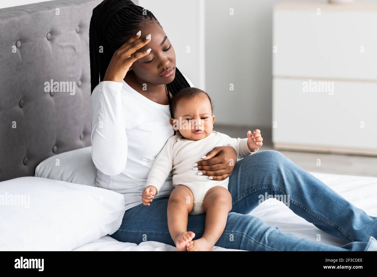 Müde afrikanisch-amerikanische Mutter sitzt mit Kind auf dem Bett Stockfoto